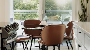A modern kitchen with a dining table and chairs, a piano, and a large window with a view of greenery. - Artsy Capitol Hill Gem City View Workspace Parking (Seattle)