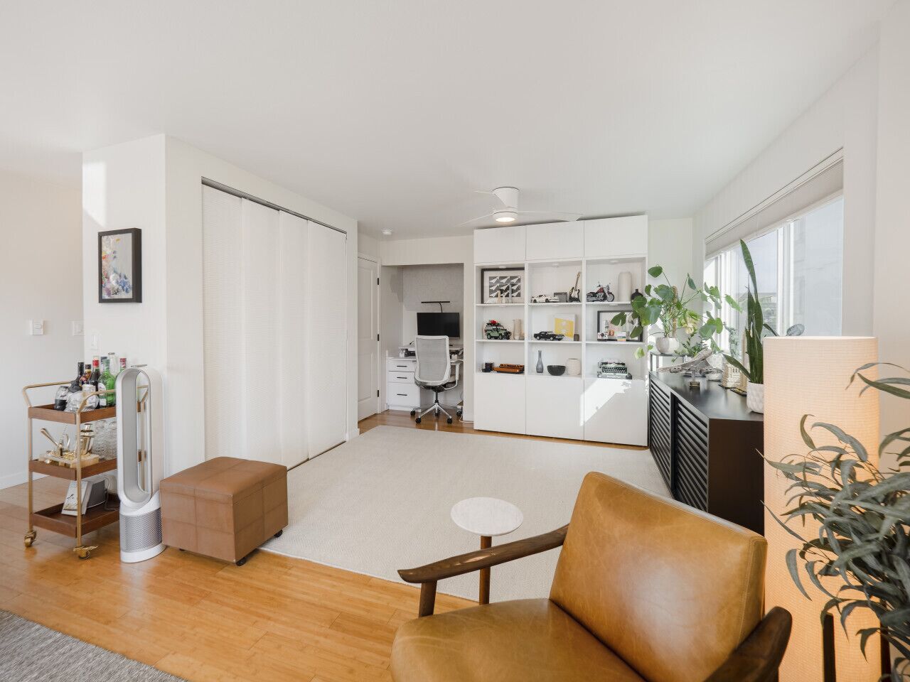 Una sala de estar moderna con un sofá de cuero, una mesa de centro y un mueble para televisor. Se observa una estantería con objetos decorativos y una planta.