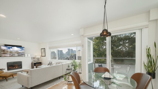 A modern living room with a glass dining table, comfortable seating, a fireplace, and large windows offering a city view. - Artsy Capitol Hill Gem City View Workspace Parking (Seattle)