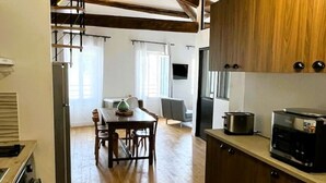 A modern kitchen with wooden cabinets, a dining area with a table and chairs, and a view of the living room. - Charming air-conditioned duplex apartment in the heart of Paris (Avignon)
