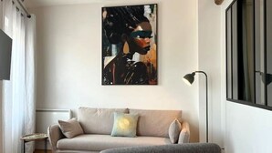 A living room with a beige sofa, a side table, and a floor lamp. - Charming air-conditioned duplex apartment in the heart of Paris (Avignon)