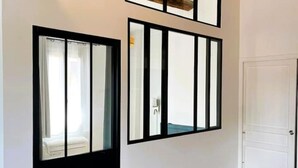 A hallway with a white door, a black-framed window, and a mirror reflecting a room with a bed and a window. - Charming air-conditioned duplex apartment in the heart of Paris (Avignon)