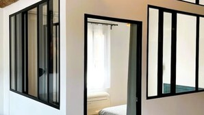 A bedroom with a bed, a window with black frames, and a white wall. - Charming air-conditioned duplex apartment in the heart of Paris (Avignon)