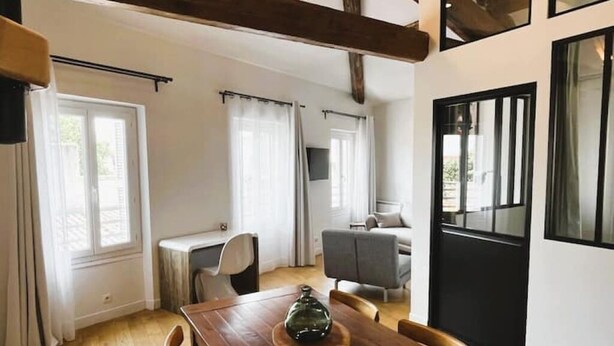 A spacious room with a wooden dining table, a grey sofa, and a large window with curtains. - Charming air-conditioned duplex apartment in the heart of Paris (Avignon)