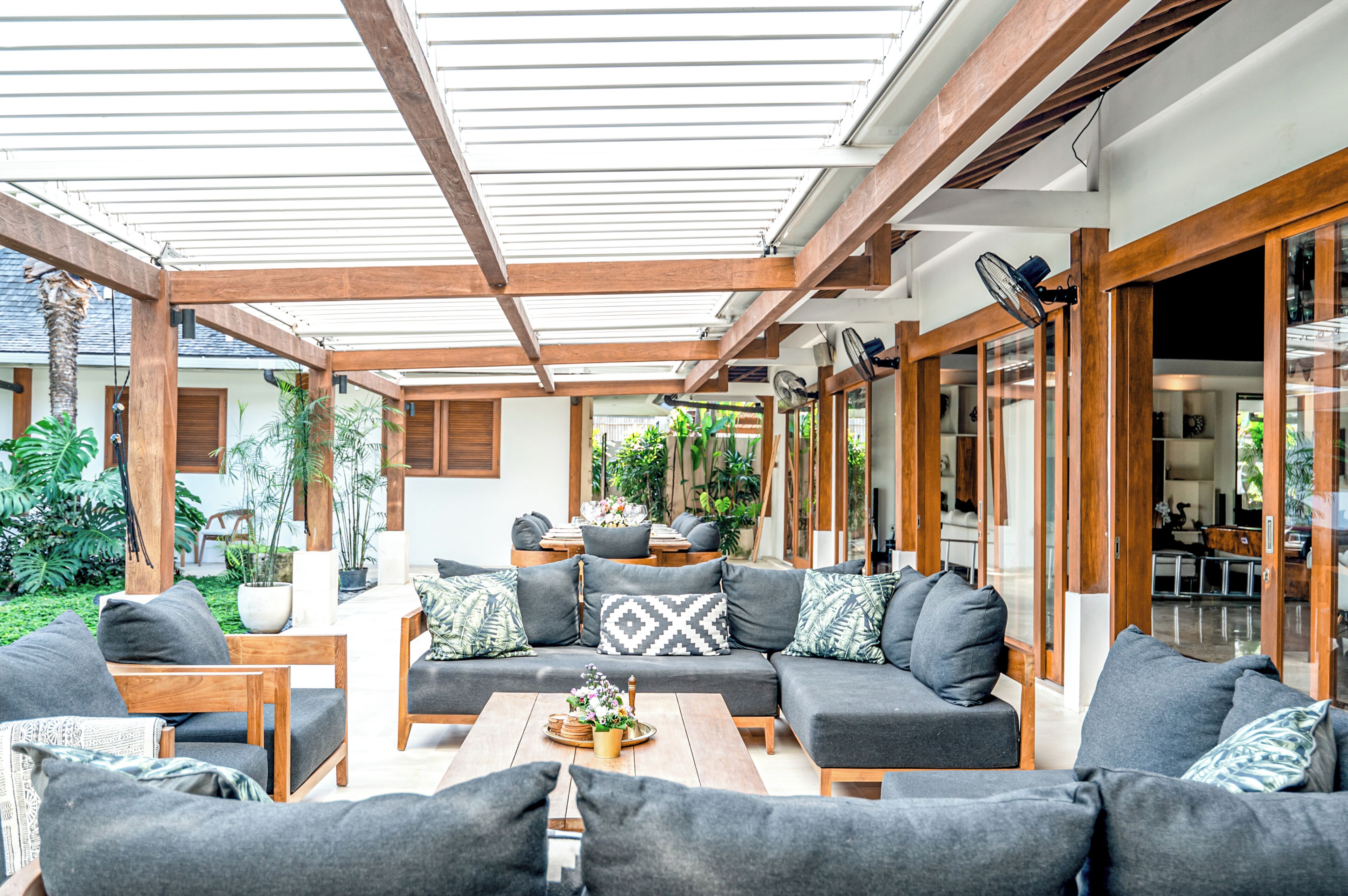 A covered outdoor seating area with wooden furniture and a glass door leading to an interior space.