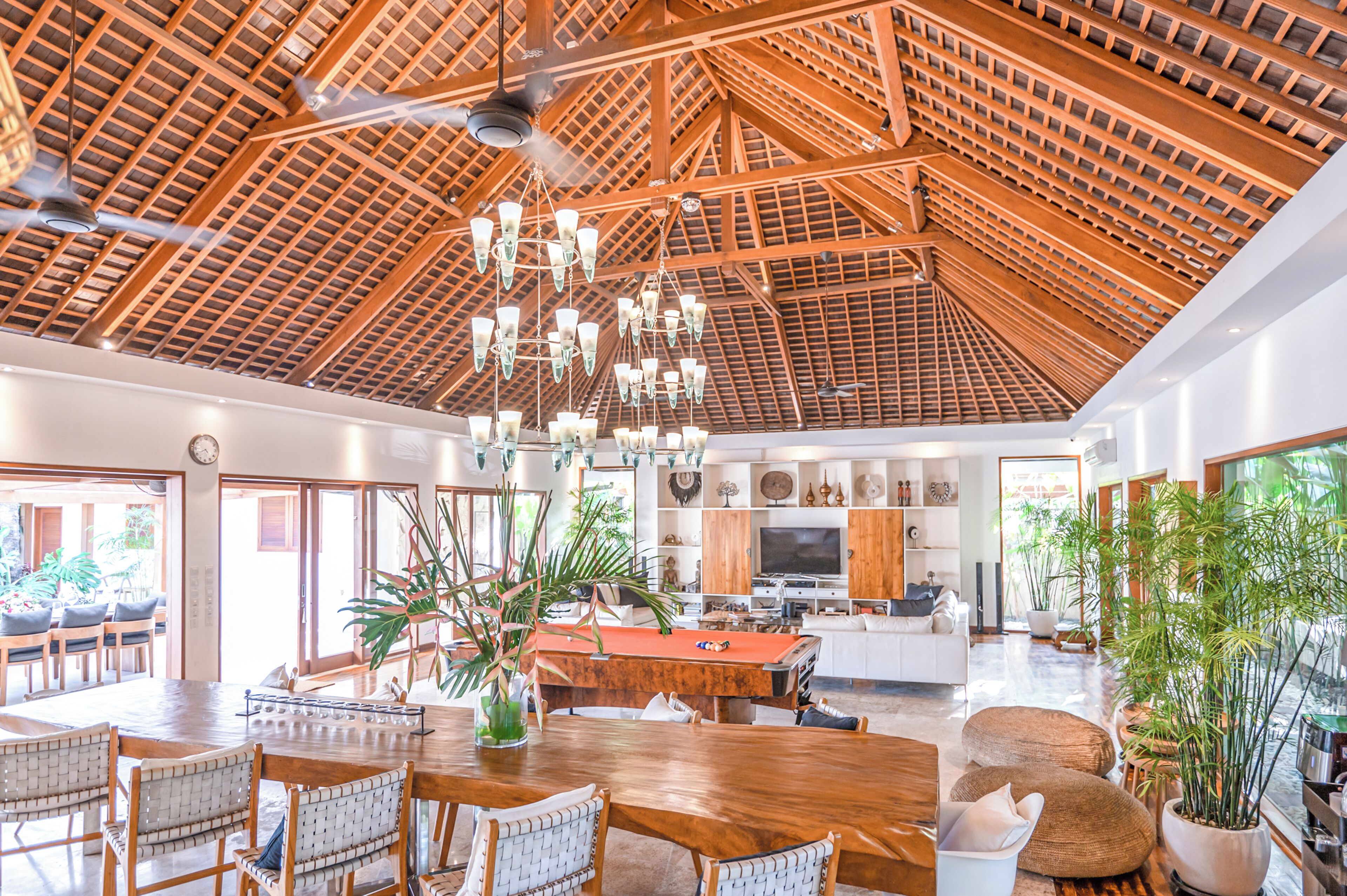 A spacious living area with a high wooden ceiling, a central wooden table, and a television.