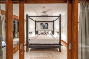 A four-poster bed with a ceiling fan, bedside lamps, and a painting on the wall.