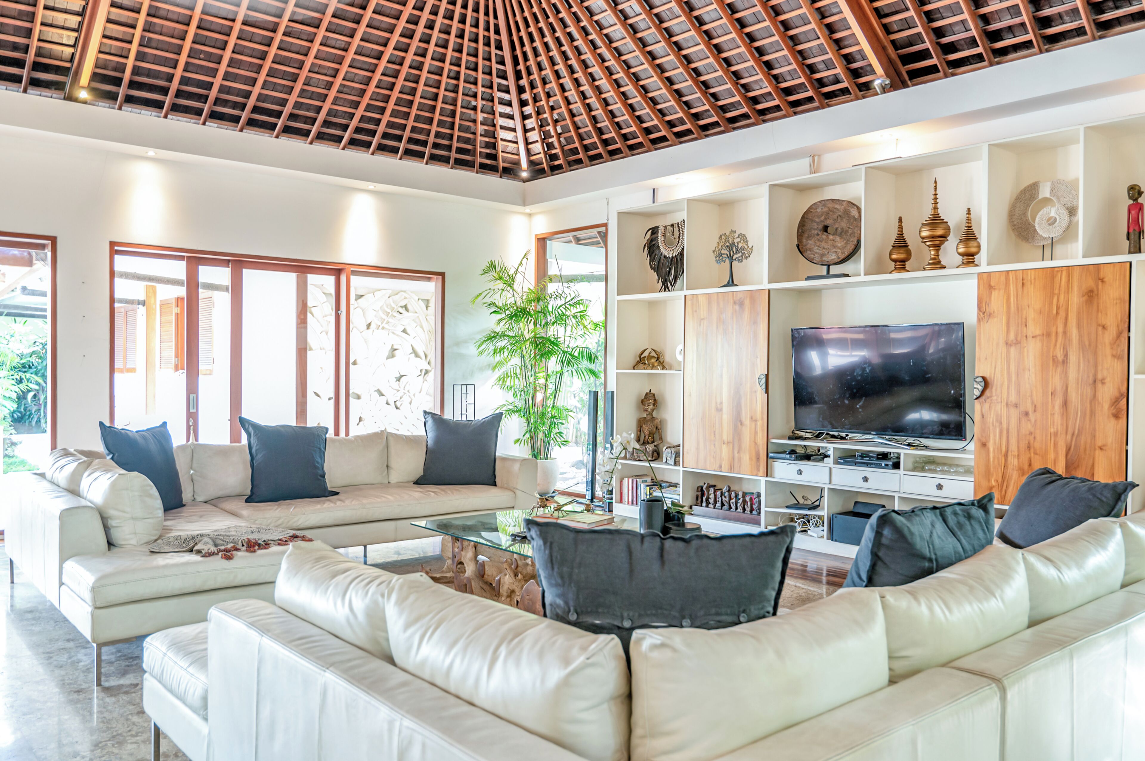 A spacious living room with a high ceiling, a large flat-screen TV, and a variety of decorative items on shelves.