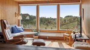 A modern interior with wooden walls, large windows, a sofa, a table, and a chair. - Well-kept 70s holiday home near the North Sea (Hvide Sande)