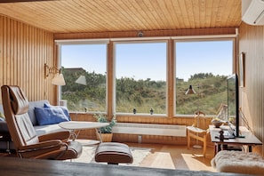 A modern interior with wooden walls, large windows, a sofa, a table, and a chair.