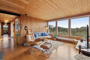 Un interno moderno con pareti rivestite in legno, un divano, una poltrona, un tavolo e ampie finestre che si affacciano sull'esterno.