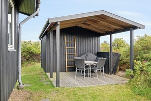En overdækket terrasse med bord og stole, en stige og et trædæk.
