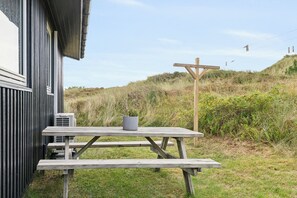 Et træbord med et potteplantestående udendørs i nærheden af en bygning med et metalhegn.