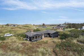 A modern house with a large deck, surrounded by natural dunes and vegetation.