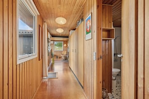 A wooden hallway with a view to a bathroom, a window, and a door leading to another room.
