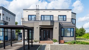 Une maison moderne à deux étages, dotée d’un balcon, de grandes fenêtres et d’un petit porche à l’avant.