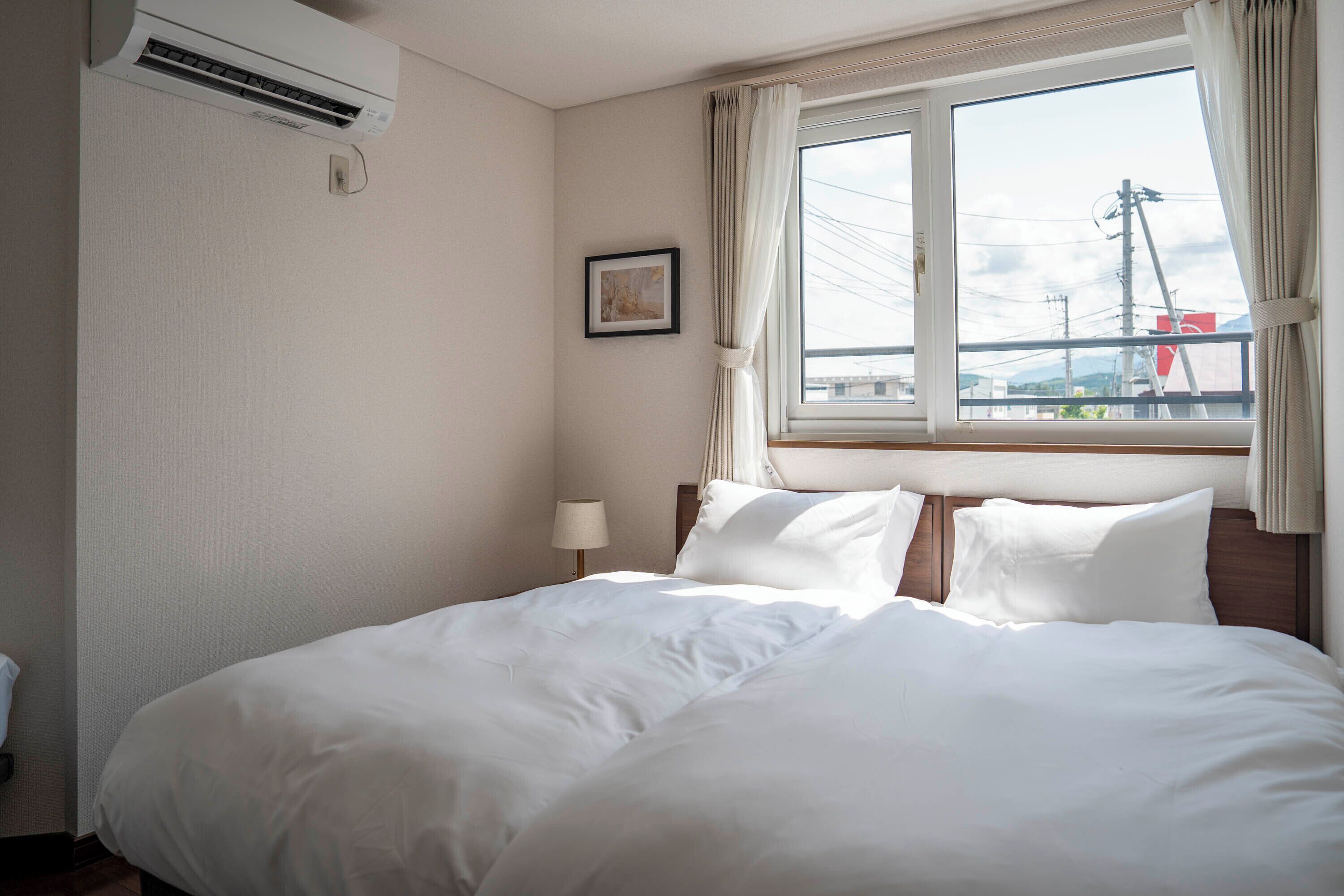 Habitación de hotel con cama, ventana con cortinas, aire acondicionado de pared y un cuadro enmarcado.