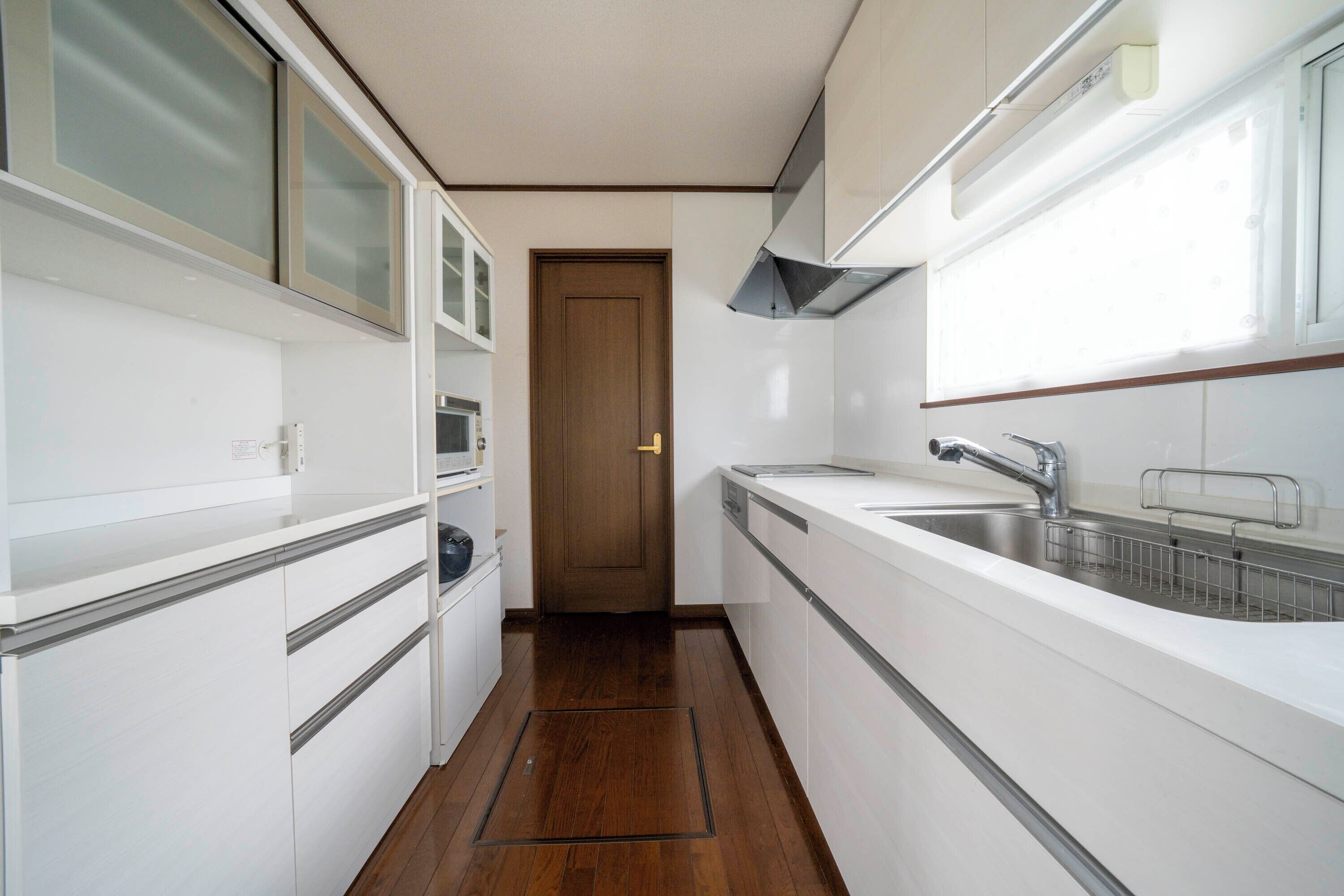 A narrow kitchen with white cabinets, a wooden door, and a stainless steel sink.
