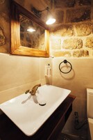 Un baño con un lavamanos blanco, un espejo con marco de madera, un tozaleto y una pared de piedra.