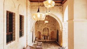 A rustic interior with exposed wooden beams, stone walls, and a stone archway leading to a courtyard.