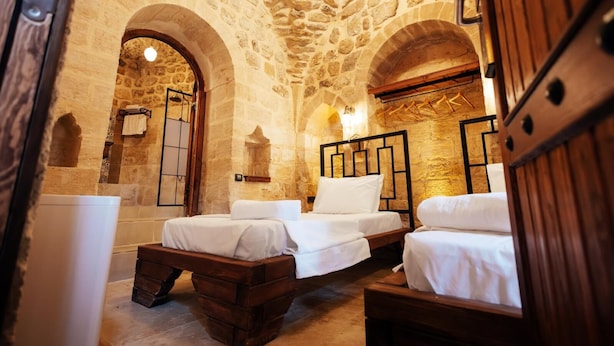 A stone-walled bedroom with three wooden beds, a bathtub, and a stone archway.