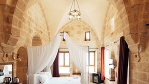 A room with a bed under a stone arch, a desk with a chair, and a radiator.