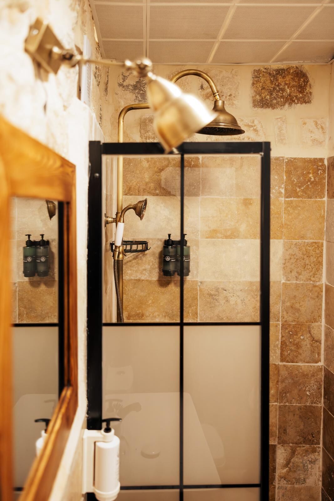 A bathroom with a glass-enclosed shower, a handheld showerhead, and a wall-mounted faucet.
