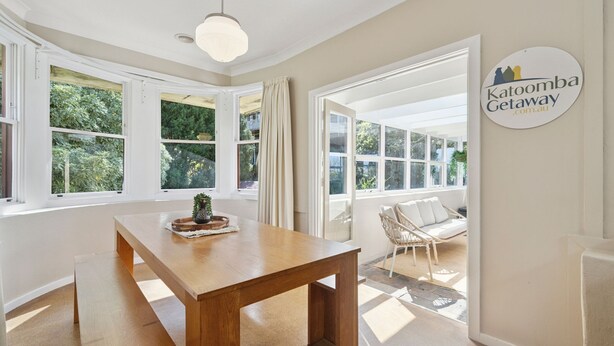 A spacious room with a wooden table, large windows, and a view of greenery outside. - Katoomba Getaway 1 -Perfectly positioned in a quiet, street just a hop, skip & jump to Katoomba town (Katoomba)