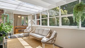 A sunlit room with a sofa, chairs, and a table, large windows with a view of greenery, and hanging plants. - Katoomba Getaway 1 -Perfectly positioned in a quiet, street just a hop, skip & jump to Katoomba town (Katoomba)