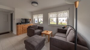 Ett modernt vardagsrum med en soffgrupp, ett soffbord i trä och en tv som står på ett träskåp.