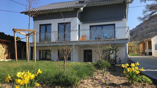 En tvåvåningsbyggnad med en balkong, en stenmur och en trädgård med gula blommor.