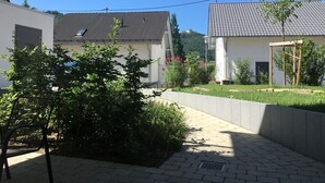 En innergård med en stenlagd gångväg, en metallbänk och ett litet träd.