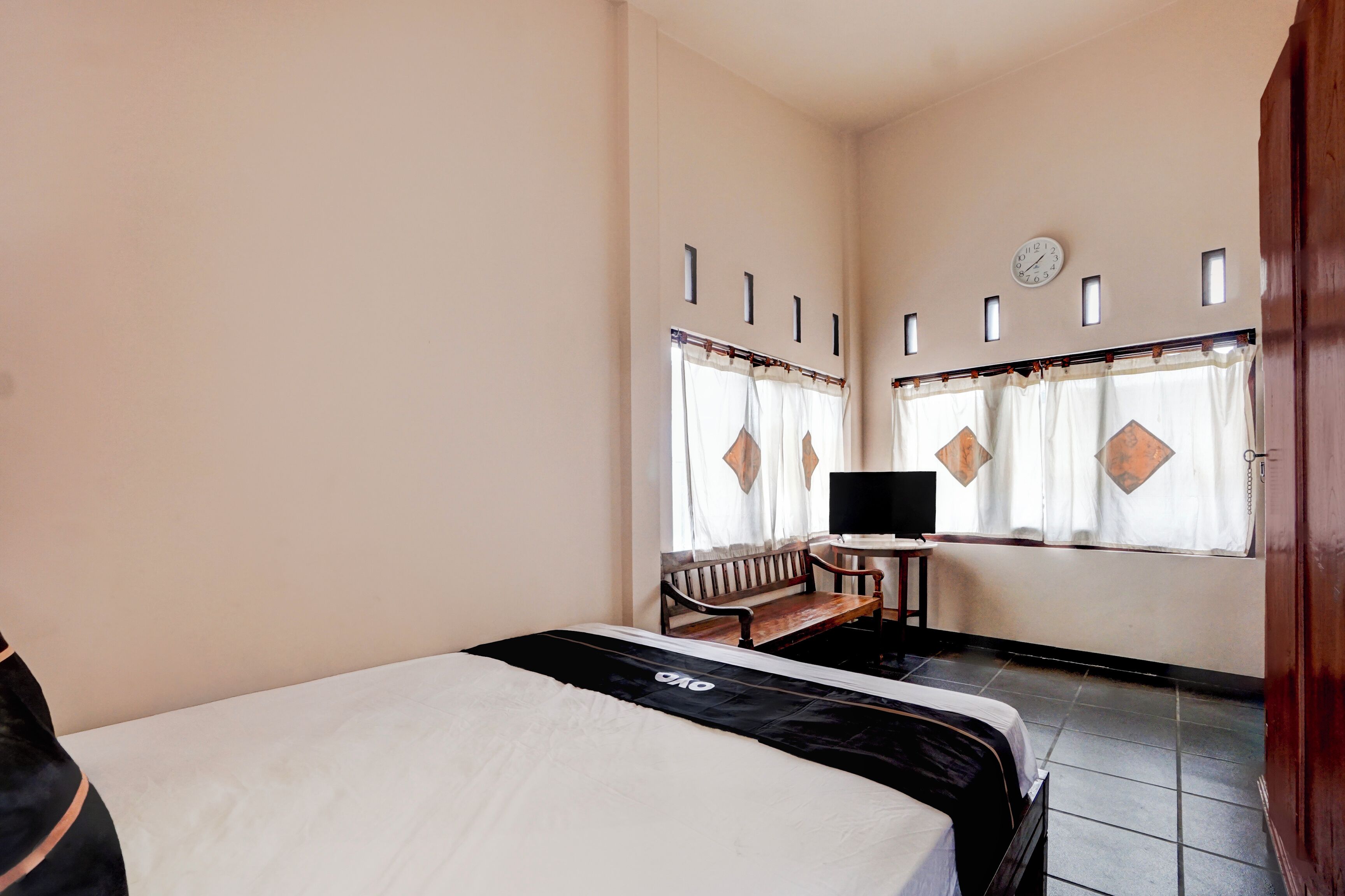 A hotel room with a bed, a desk, a chair, a clock, and a window with curtains.