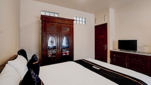 Une chambre d’hôtel avec un lit, une télévision, une armoire et une fenêtre avec des rideaux.