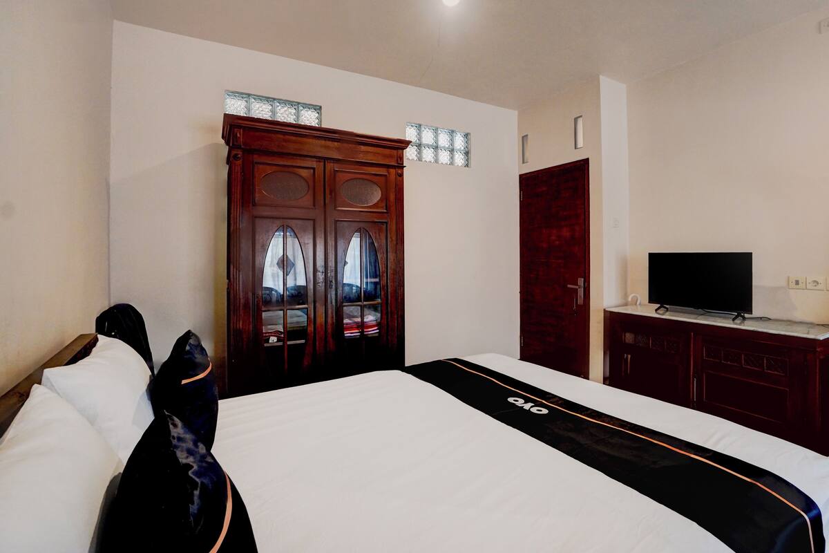 Una habitación de hotel con cama, televisión, armario y ventana con cortinas.