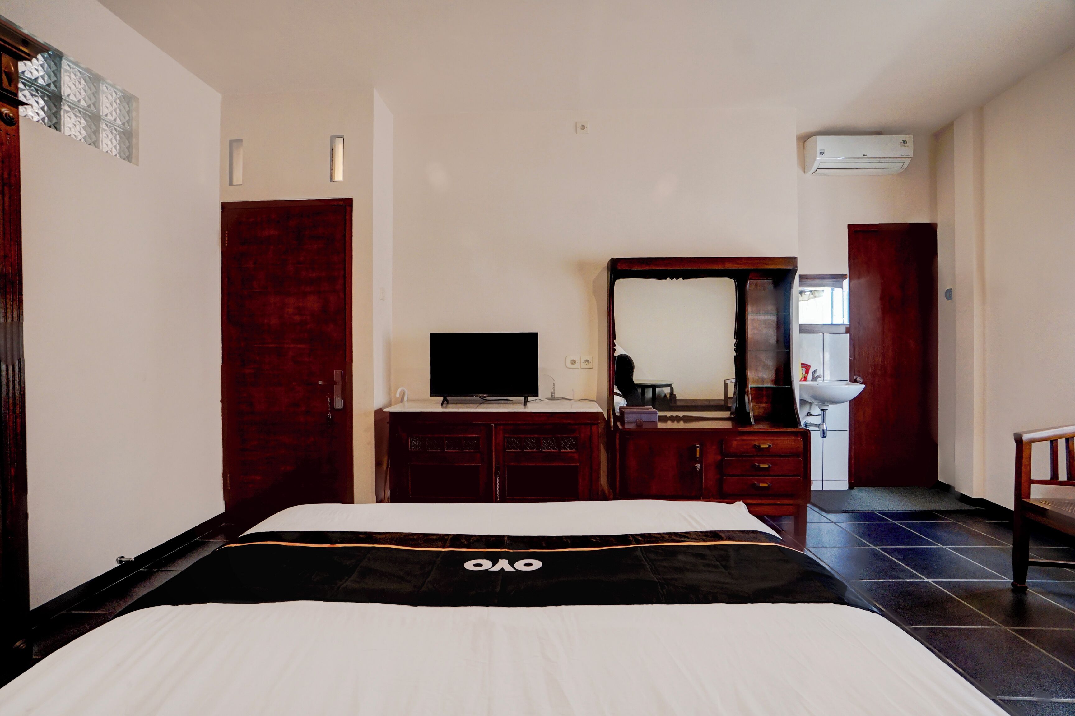 A hotel room with a bed, a TV, a dresser, a mirror, and a bathroom visible in the background.