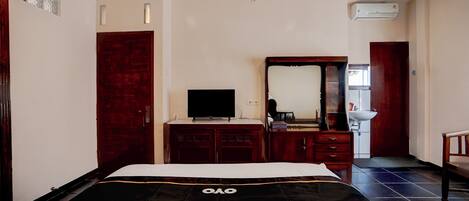 A hotel room with a bed, a TV, a dresser, a mirror, and a bathroom visible in the background.
