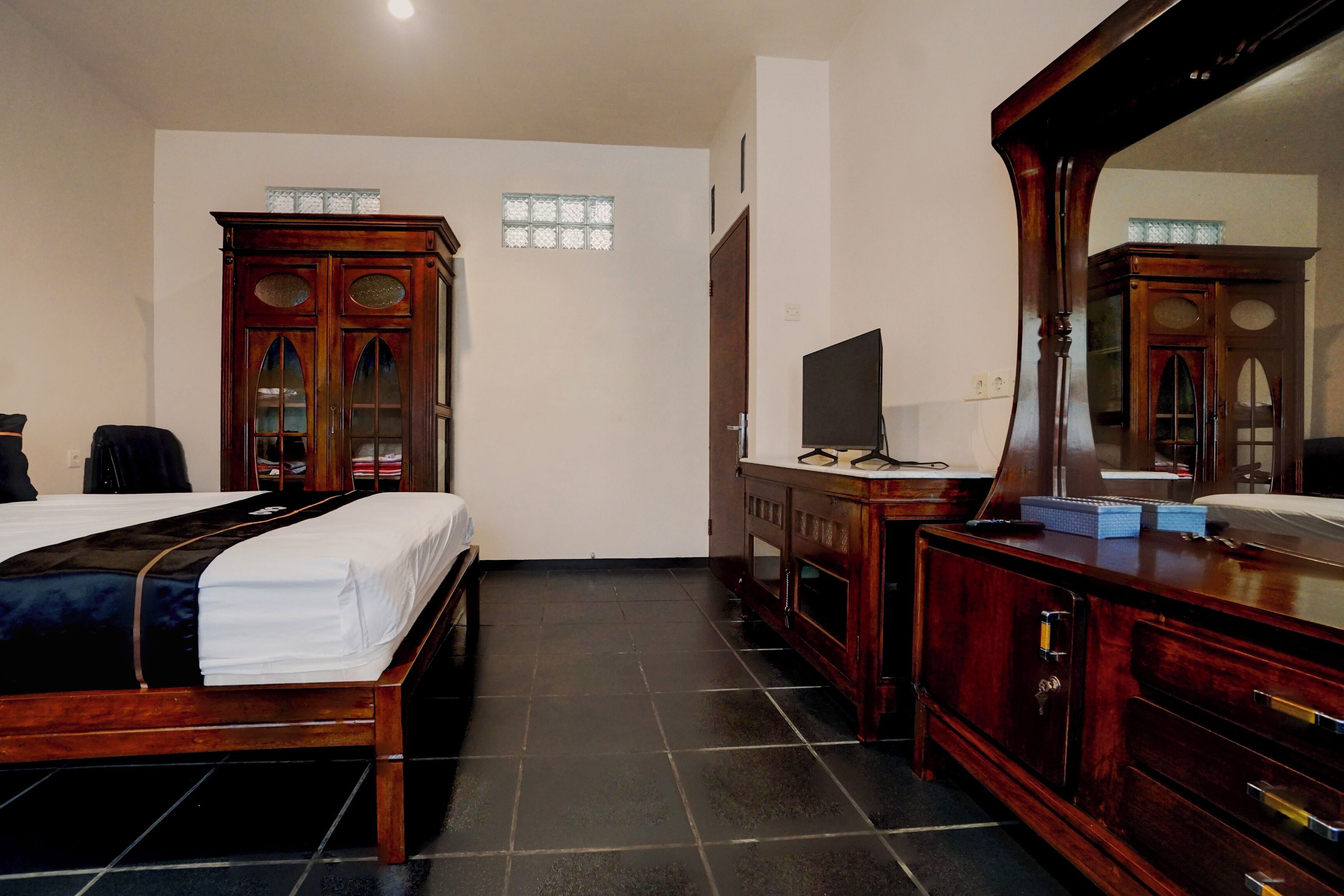 Una camera d'albergo con un letto di legno, una cassettiera, una televisione e uno specchio.