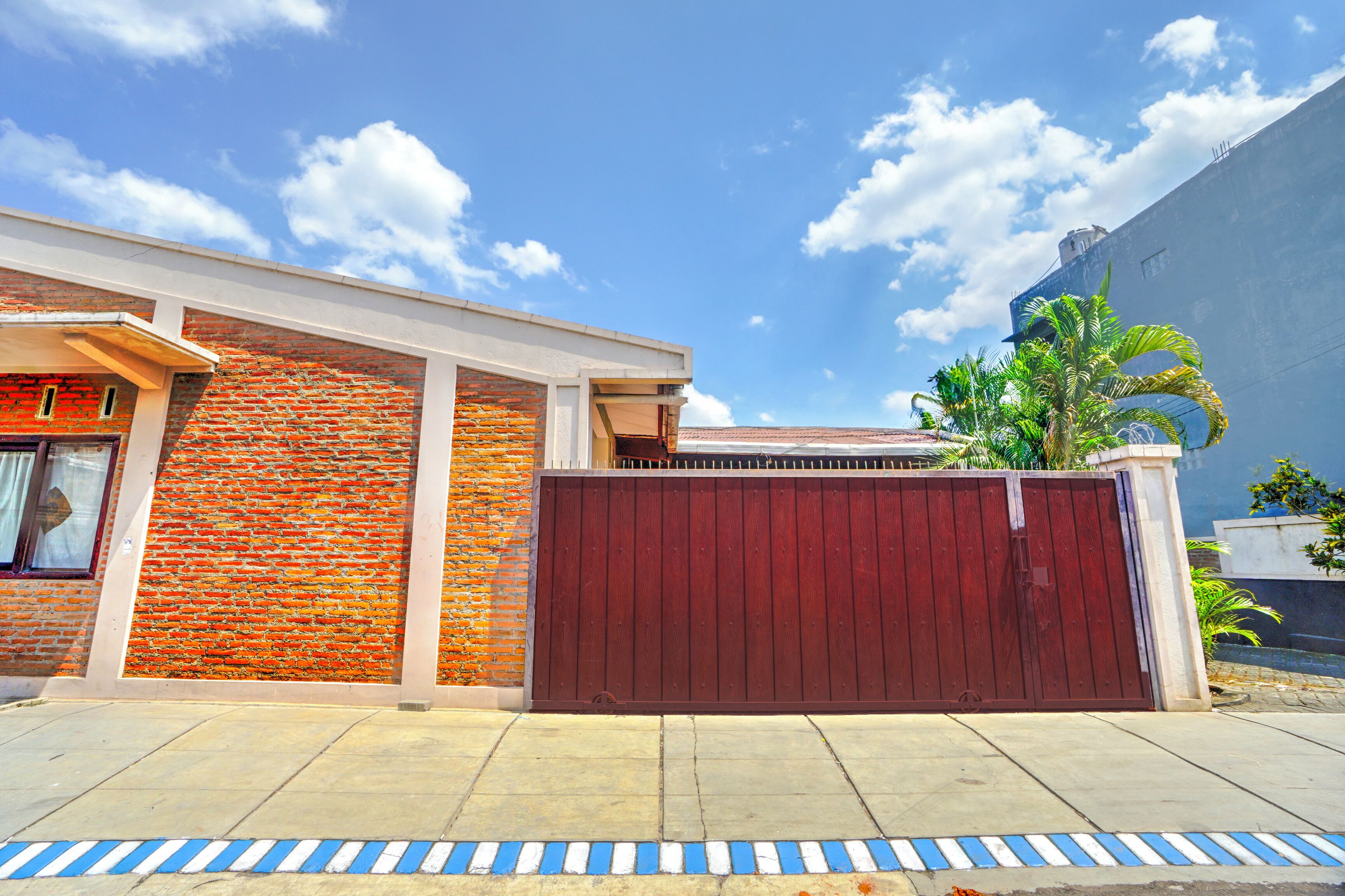 A residential building with a brick facade, a red gate, and a clear blue sky.
