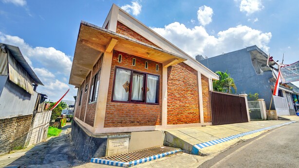 Une petite maison en briques avec un toit en pente, un porche à l’avant et une fenêtre bien visible.