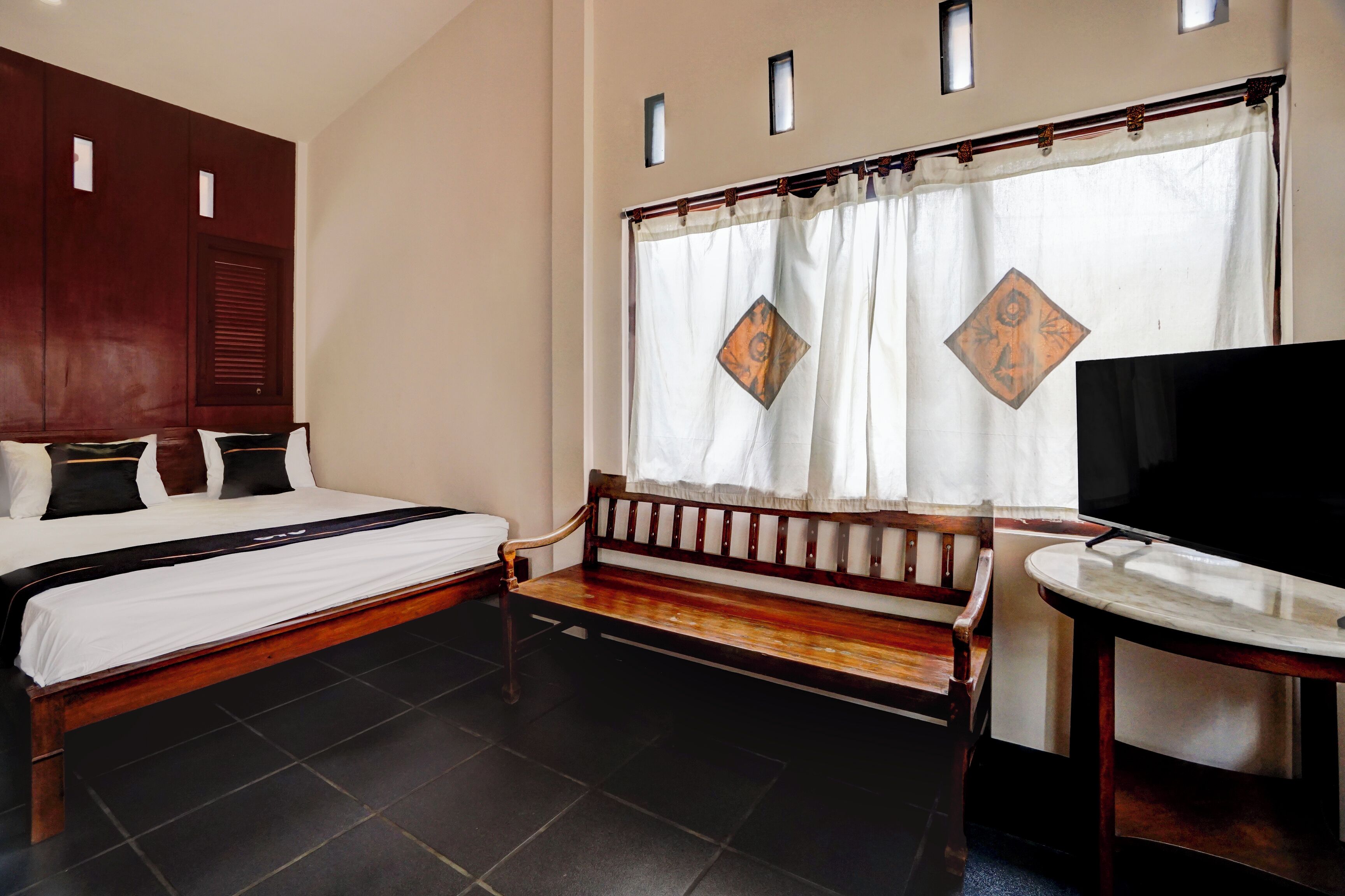 Habitación de hotel con una cama grande, un banco, un televisor y una ventana con cortinas.