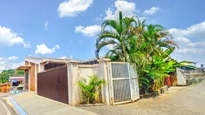 Un quartier résidentiel doté d’une entrée sécurisée, de trottoirs pavés et d’une végétation luxuriante, notamment des palmiers.
