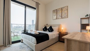 A modern bedroom with a large bed, a wooden nightstand, a desk, and a balcony with a city view. - Binghatti Heights Residences- JVC (Dubai)