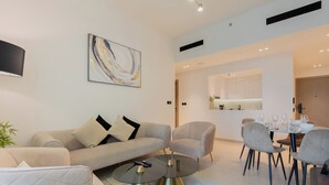 A modern living room with a sofa, armchairs, a glass coffee table, and a dining area with chairs and a table. - Binghatti Heights Residences- JVC (Dubai)
