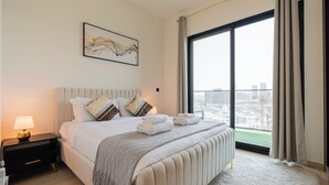 A modern hotel room with a large bed, a nightstand, a lamp, and a city view through a large window. - Binghatti Heights Residences- JVC (Dubai)