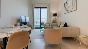 A modern living room with a dining area, a sofa, a TV, and a balcony with a view of buildings. - Binghatti Heights Residences- JVC (Dubai)