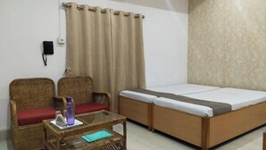A room with a bed, two wicker chairs, a small table with a bottle and a notebook, and a curtain. - The Executive Inn (Guwahati)