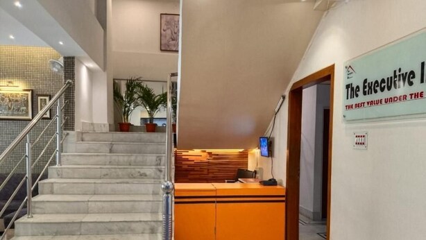 A reception area with a marble staircase, a reception desk, and a sign reading "The Executive". - The Executive Inn (Guwahati)