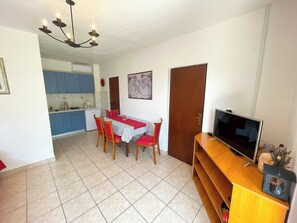 A compact living space with a dining area, kitchenette, and a television on a wooden stand.