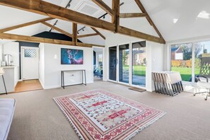 A spacious room with a high ceiling, wooden beams, a large window, a patterned rug, and a painting on the wall. - Spacious 6-Bed Home Surrounded by Nature (Lincolnshire)